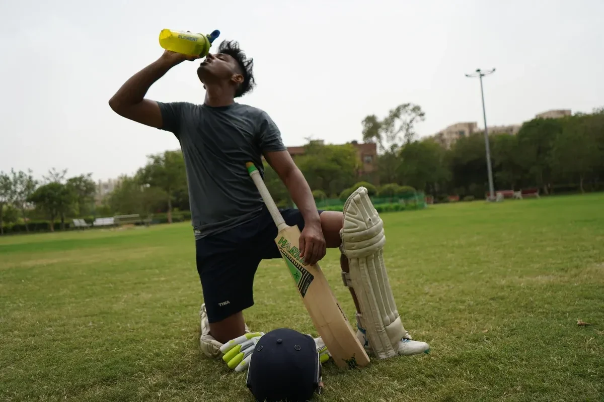 Cricket player outside on the pitch drinking a bottle of water