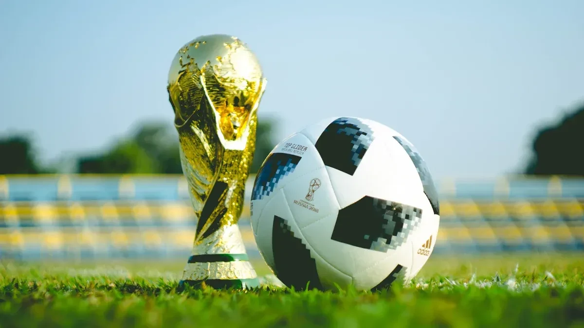 The FIFA World Cup trophy on the grass next to a soccer ball