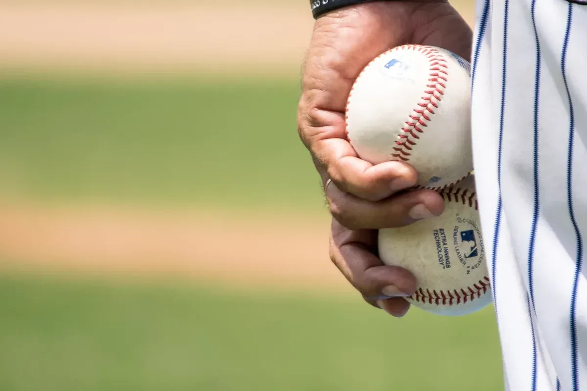 A baseball player on the pitch with two baseballs in hand