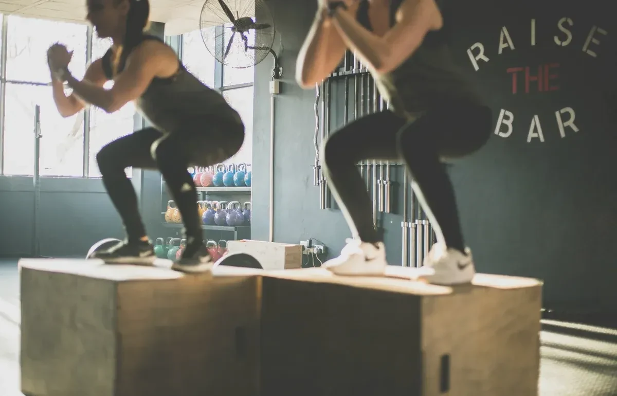 Two women box jumping in a gym