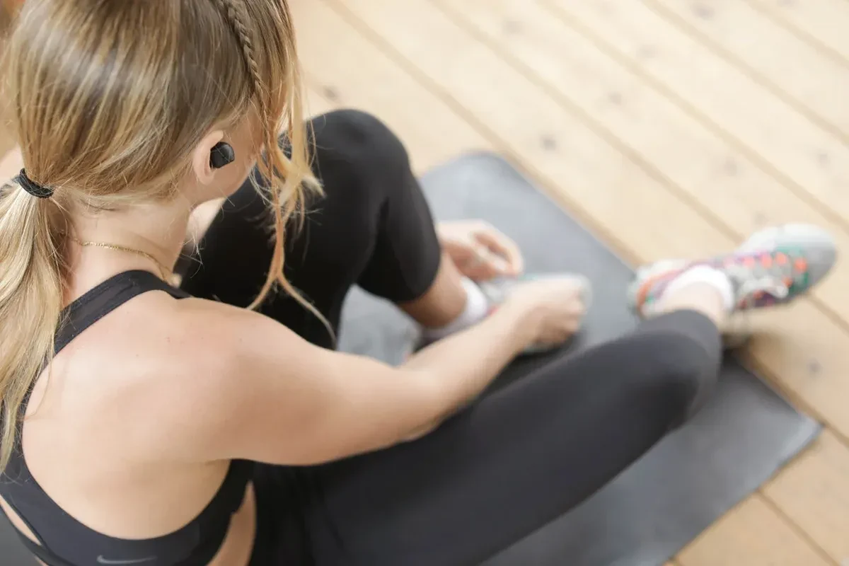 A woman on a yoga mat lacing up her shoes before she/ exercises